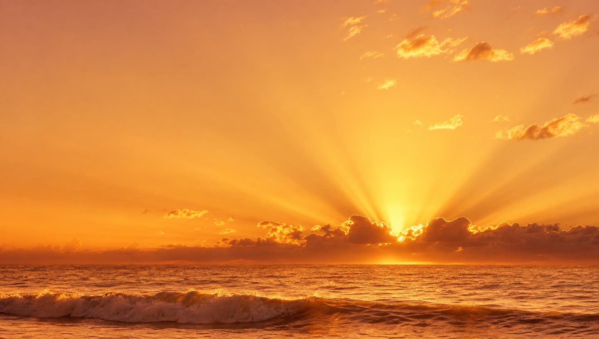 Sunrise over the Gulf of Mexico, golden light spreading from behind a low cloud above calm water.