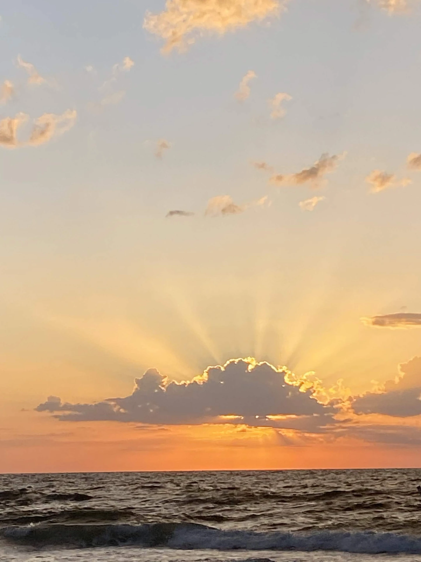 Sunrise rays fanning out from behind a single low cloud over the Gulf